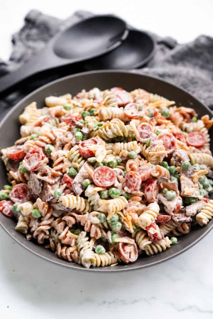 A serving bowl is filled with creamy bacon ranch pasta salad.