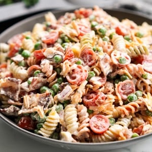 Close up picture of Creamy Bacon Ranch Pasta Salad filled with pasta, peas, crispy bacon, cherry tomatoes, red onions, shredded cheddar cheese, and ranch dressing.