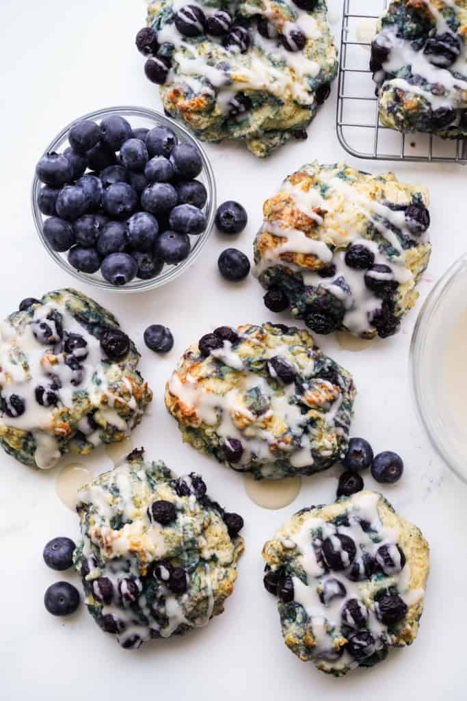A small bowl full of plump blueberries is surrounded by delicious blueberry biscutis.