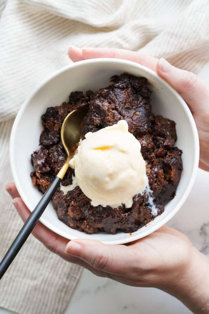 A bowl full of Brownie Pudding Cake is topped with vanilla ice cream and ready to eat.