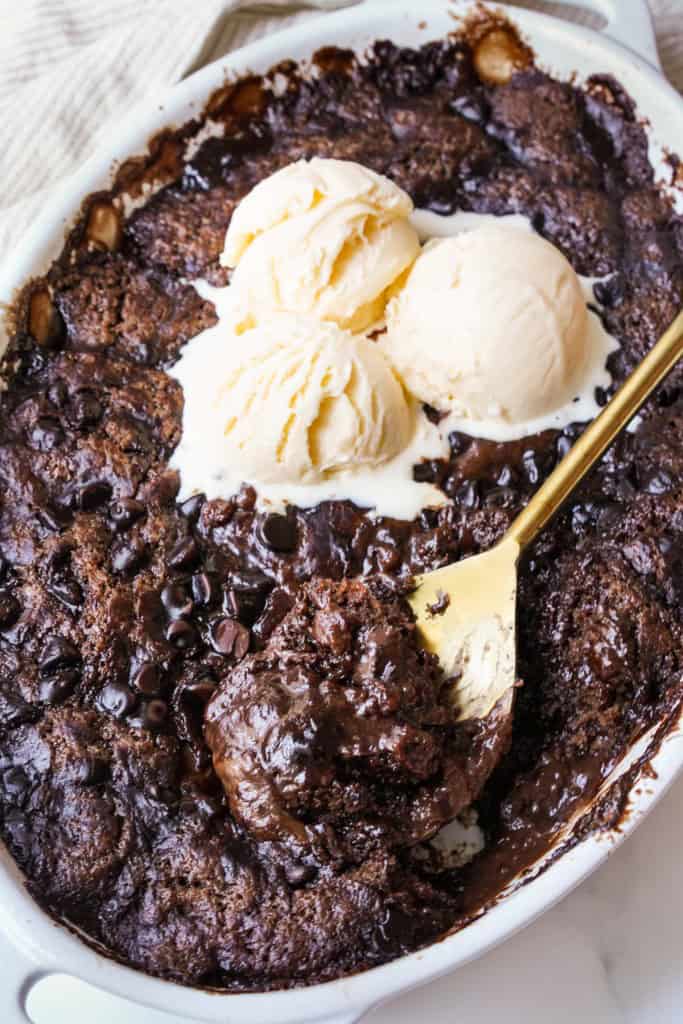 A spoon is scooping our a portion of Chocolate Pudding Cake that has been topped with 3 scoops of vanilla ice cream.