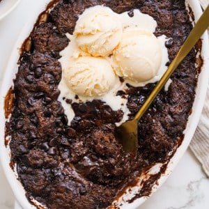 Gooey chocolate pudding cake is being scooped out of an oval baking dish.
