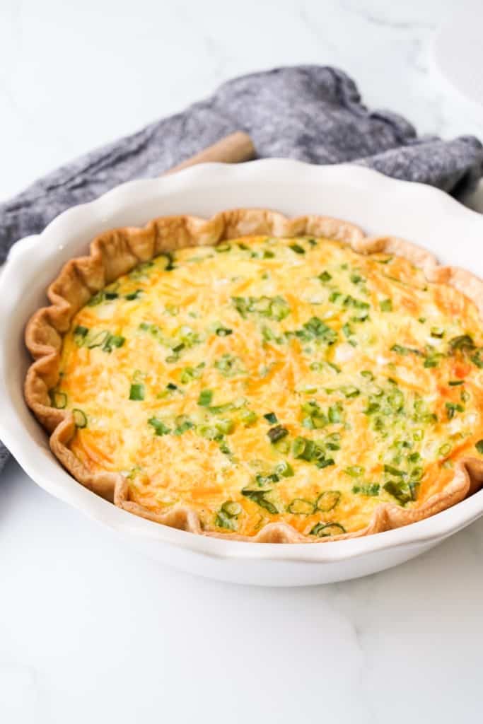 Ham and cheese quiche with heavy cream is in a pie pan.