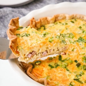 A slice of Ham and Cheese quiche is being lifted from a pie pan.