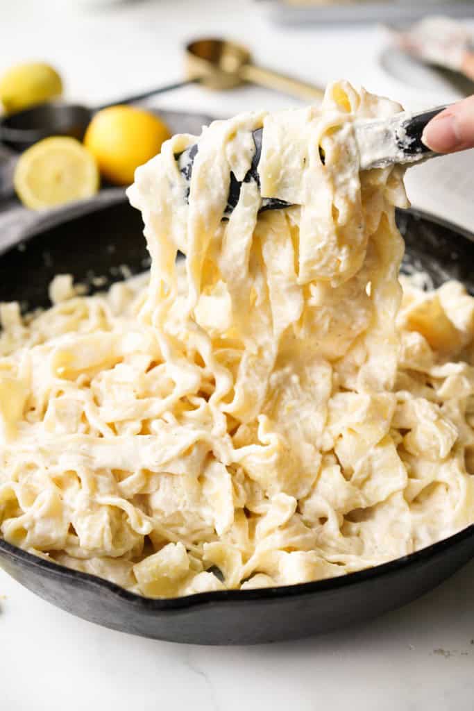 Tongs are lifting Lemon ricotta pasta from a cast iron pan.
