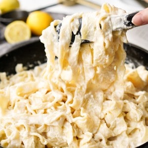Close up picture of thick noodles coated in a lemon ricotta sauce being lifted from a cast iron.