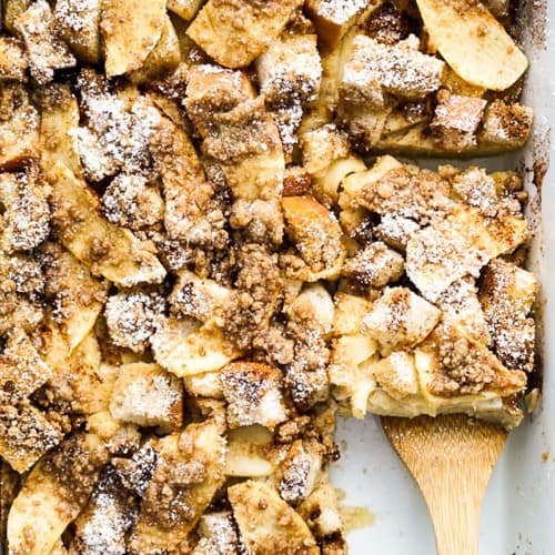 Lifting up French toast casserole topped with apples and crumbles from a dish