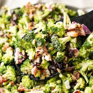 A spoon full of Broccoli Salad with Bacon is being lifted out of a bowl.