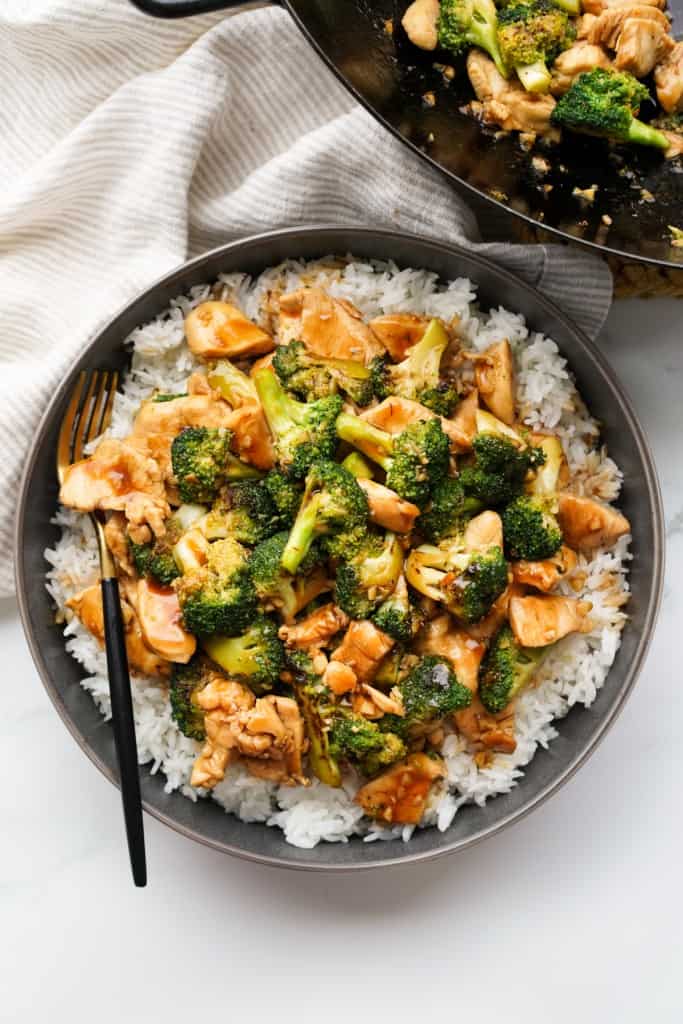 A black bowl is filled with rice topped with Chicken and Broccoli Stir Fry.