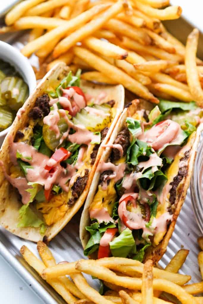 Two hamburger tacos are on a tray along with french fries.