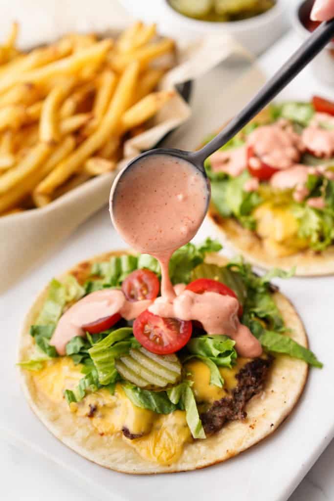 Burger sauce is being drizzled over a Cheeseburger taco.