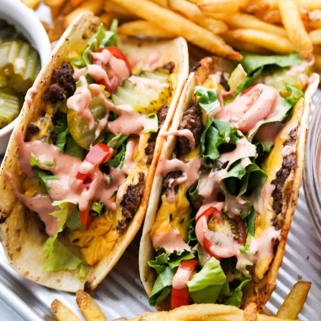 Close up picture of two cheese burger tacos stuffed full of burger toppings and burger sauce.