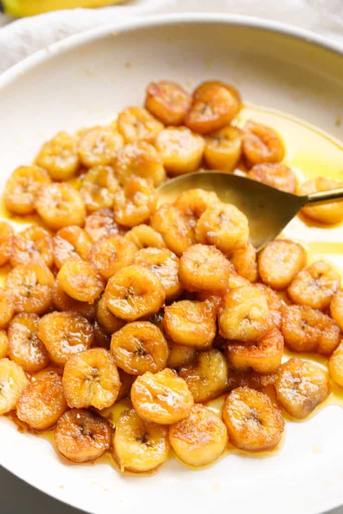 A spoon is lifting caramelized bananas from in a skillet.