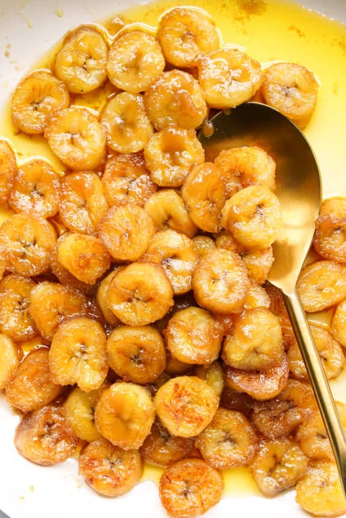 A spoon is scooping up candied bananas from a skillet.
