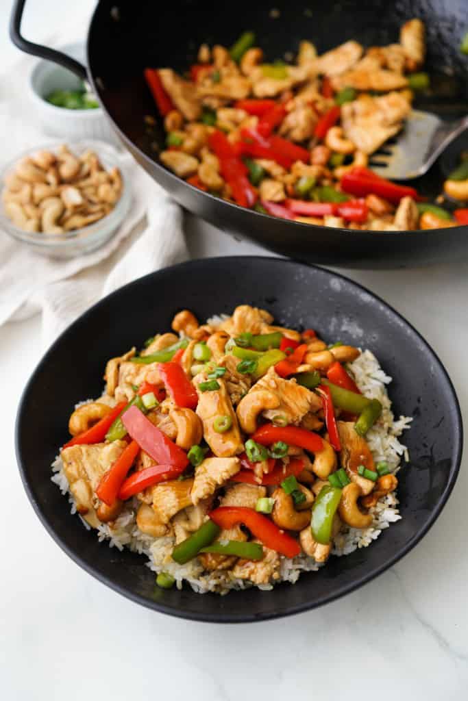 A black bowl is filled with rice that has been topped with a delicious Chicken with nuts.