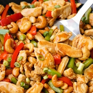 A spoon is scooping up chicken with cashew nuts.