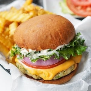 A ground chicken burger patty is topped with melted cheese, lettuce, tomato, onion, and mayonnaise.