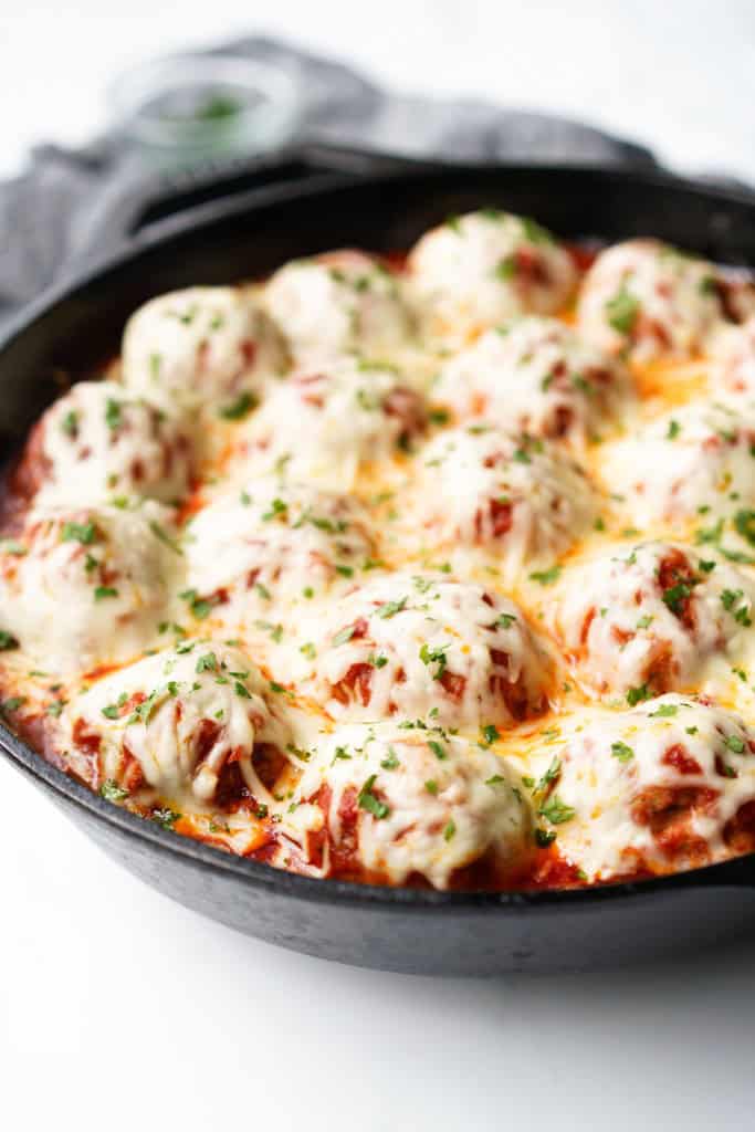 A closer picture of a cast iron skillet filled with Chicken Parmesan Meatballs coated in melted mozzarella cheese.