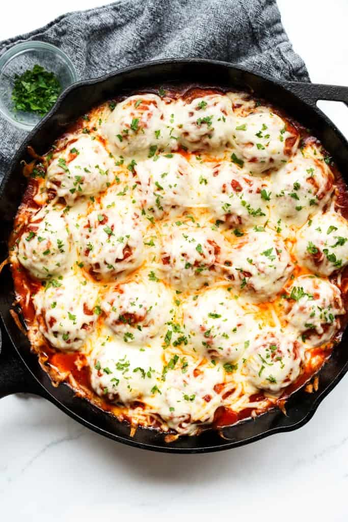 A cast iron skillet is filled with chicken parm meatballs topped with melted mozzarella cheese.