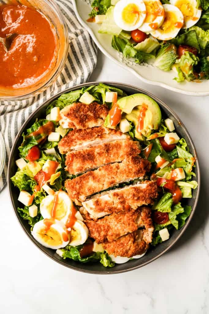 A large bowl of salad topped with a piece of crispy chicken breast, topped with dressing