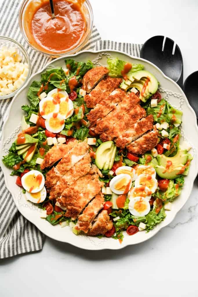 A large platter of salad topped with two pieces of sliced crispy breaded chicken