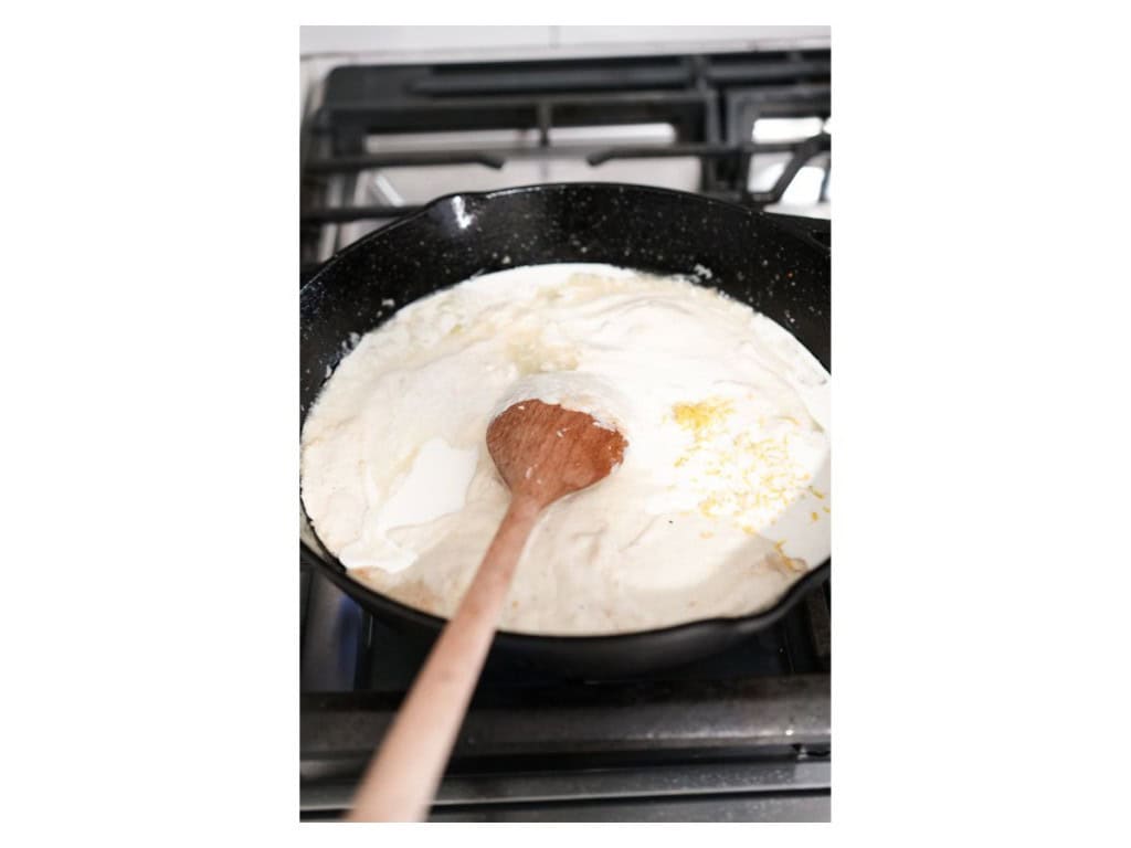 Lemon juice and zest is added to a cast iron skillet filled with a melted ricotta cheese sauce.