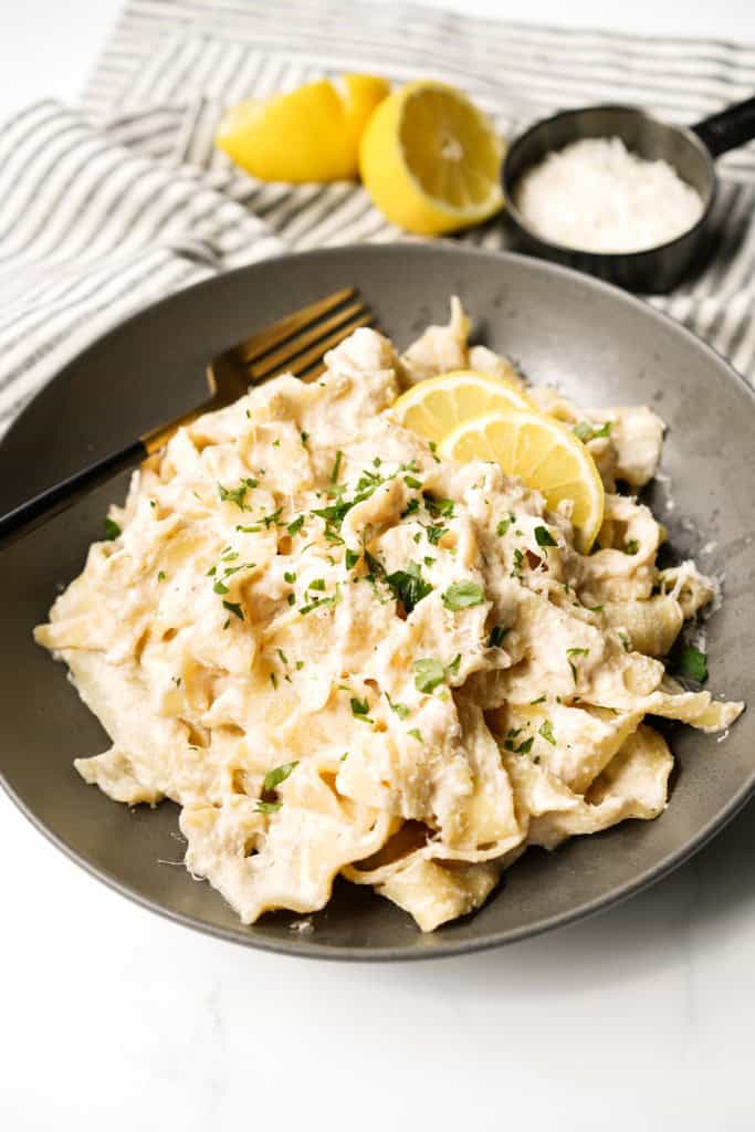 A plate of lemon ricotta pasta topped with parsley and lemon wedges on the side