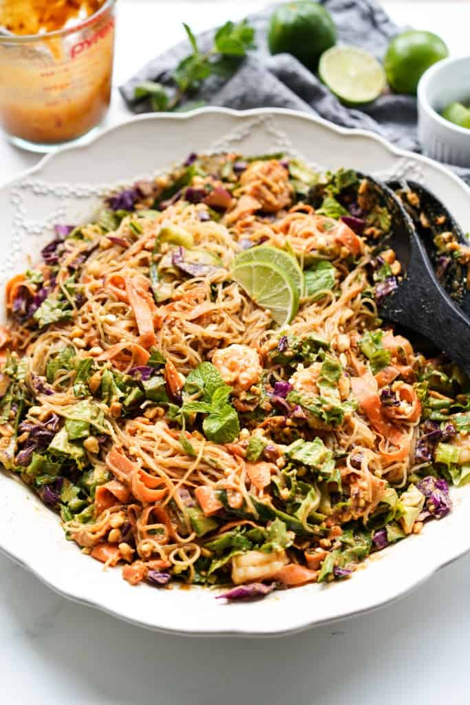 A white bowl is filled with Spring Roll Salad packed full with crunchy veggies, chewy noodles, and delicious shrimp all topped with a yummy peanut butter sauce.