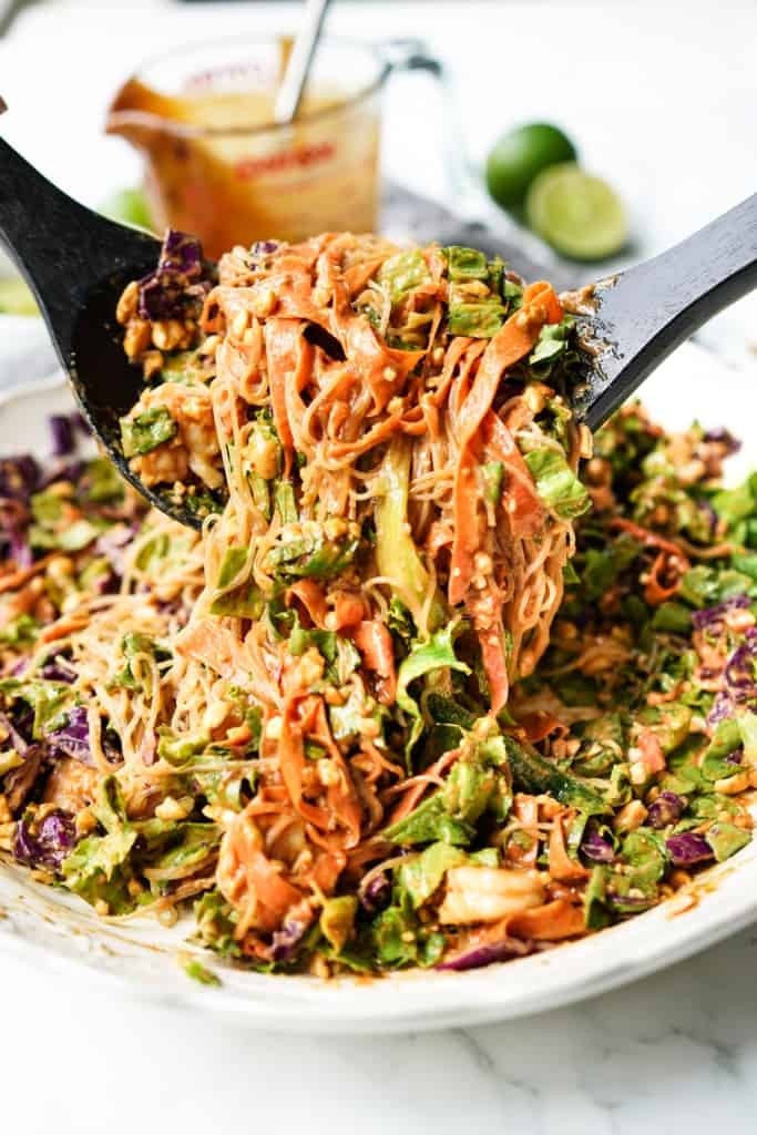Salad utensils are lifting up Vietnamese spring roll salad out of a white bowl.