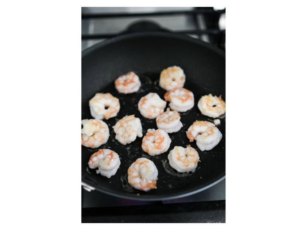Shrimp are almost fully cooked in a skillet over medium-high heat.