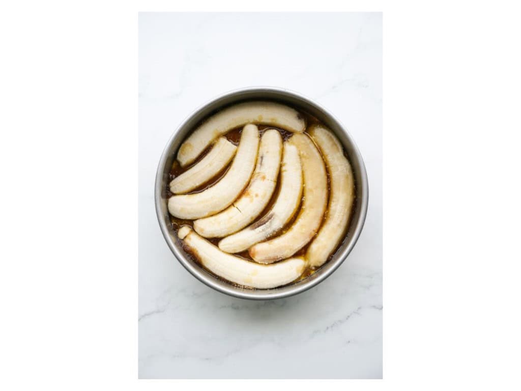 Halved bananas are added to the cake pan.