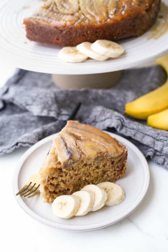 A slice of caramel banana cake is on a small plate along with sliced bananas.