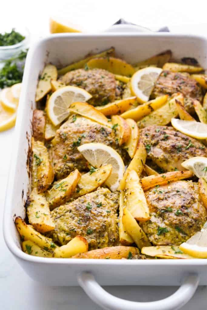 Fresh out of the oven, a baking dish holds juicy Greek chicken thighs and sliced potatoes.