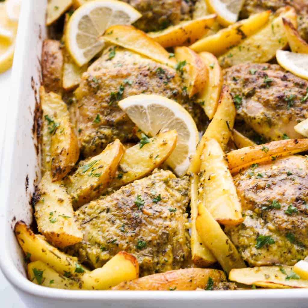 A rectangular baking dish is filled with Greek Lemon Chicken Thighs and potatoes.