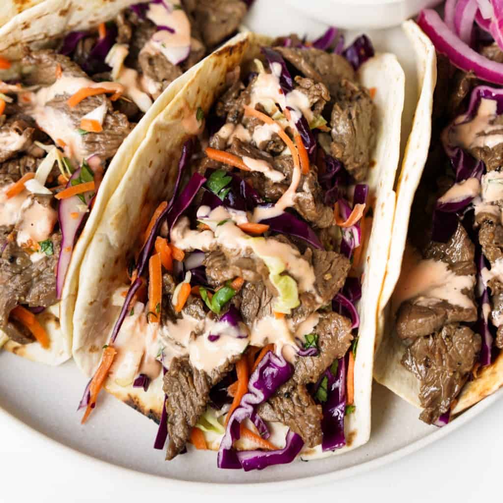 A Korean BBQ Beef Taco stuffed with slaw and beef topped with a sriracha mayo drizzle.