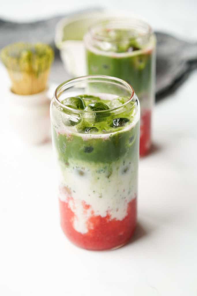 Making a strawberry matcha latte by layering strawberry puree, milk, and matcha in a glass with ice.