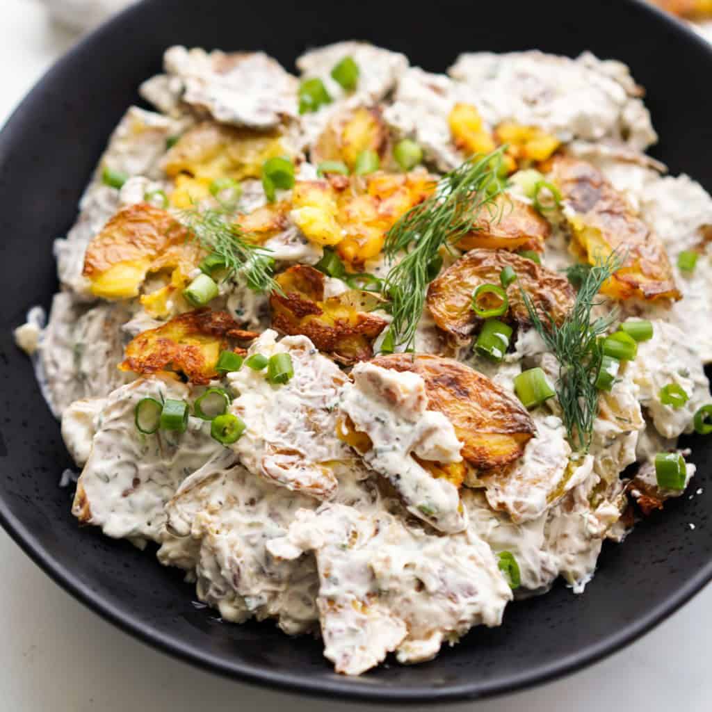A close up picture of crispy smashed potato salad in a black bowl.