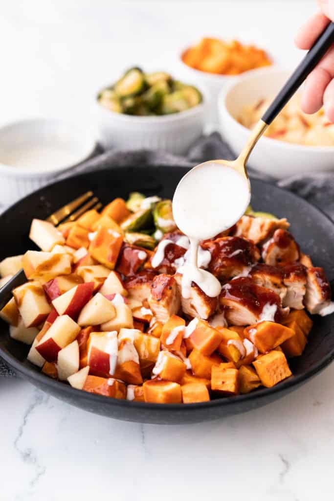 Ranch dressing is drizzled over sheet pan BBQ chicken sweet potato bowl.