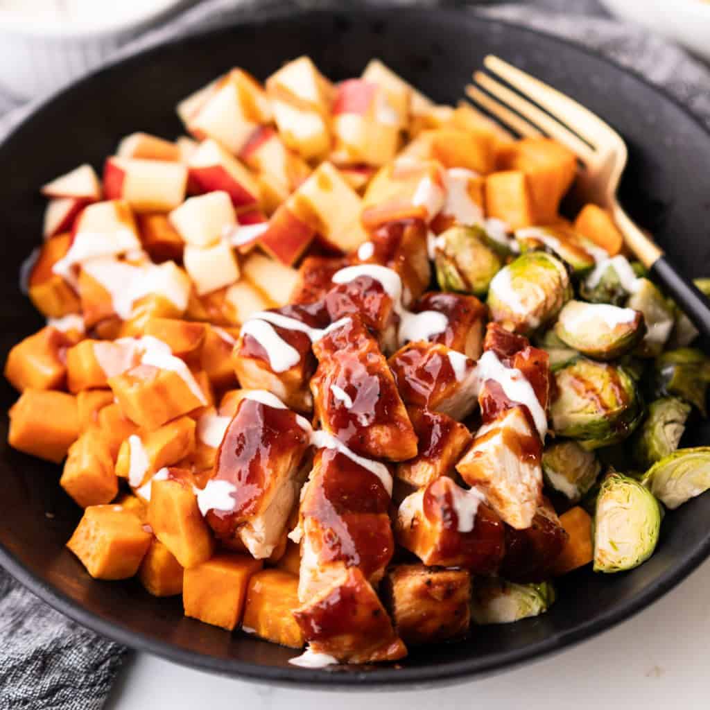Sheet pan BBQ chicken, sweet potatoes, brussels sprouts and apples are in a bowl and ready to be eaten.