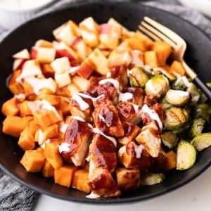 Sheet pan BBQ chicken, sweet potatoes, brussels sprouts and apples are in a bowl and ready to be eaten.