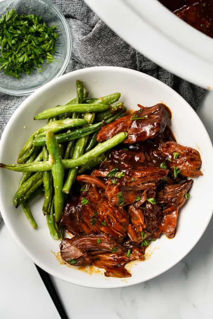 Slow cooker BBQ chuck roast is plated with a side of green beans.