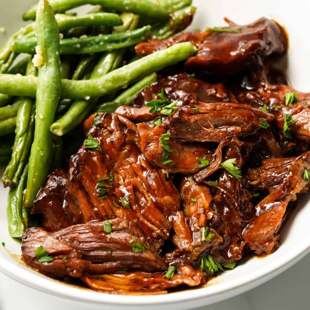 Saucy shredded barbecue beef is on a plate with a side of green beans.