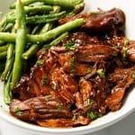 Saucy shredded barbecue beef is on a plate with a side of green beans.