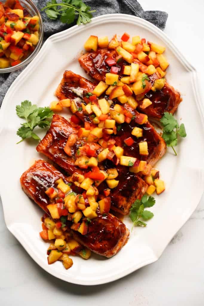A serving platter has four BBQ salmon filets topped with peach salsa.