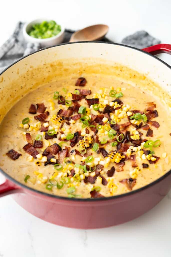 A red Dutch oven is filled with a creamy Potato Corn Soup.