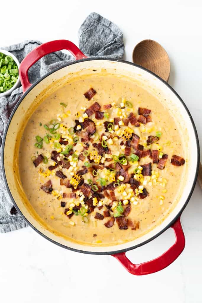 Corn Chowder with potatoes is garnished with green onions and diced bacon.
