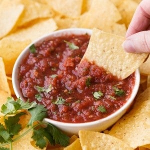 A chip is scooping up some fresh tomato salsa out of a small bowl.