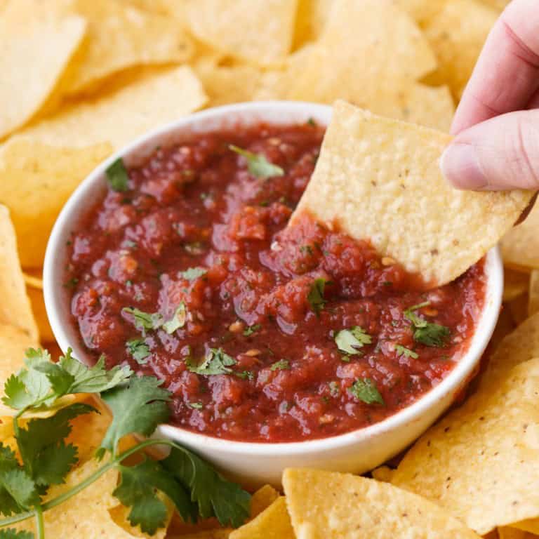 A chip is scooping up some fresh tomato salsa out of a small bowl.