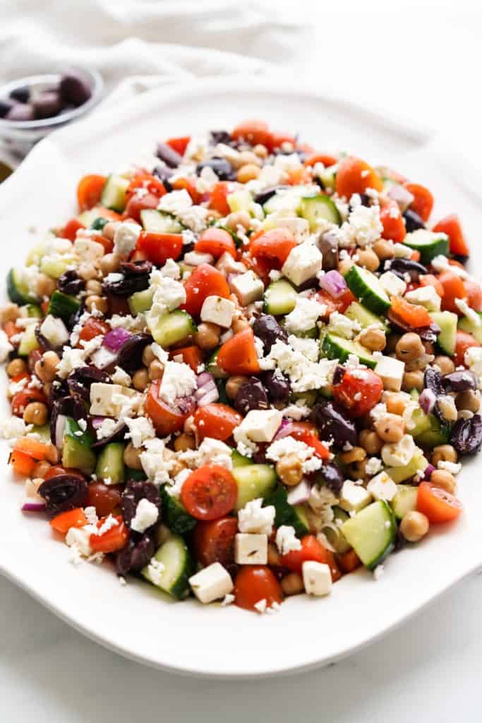 Greek garbanzo bean salad is topped with crumbled feta cheese and served on a platter.