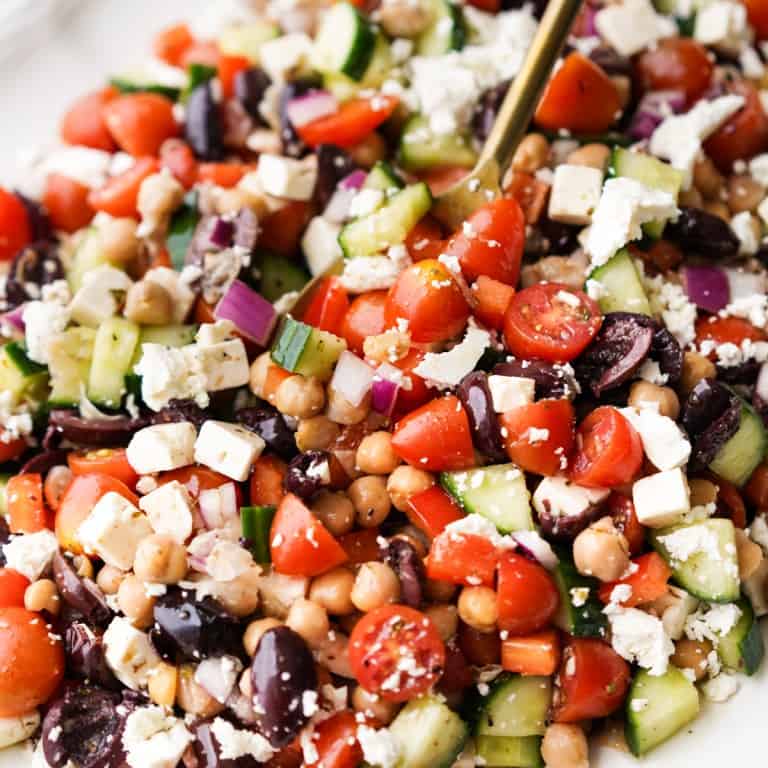 A close up picture of a spoon scooping up a salad with chickpeas.